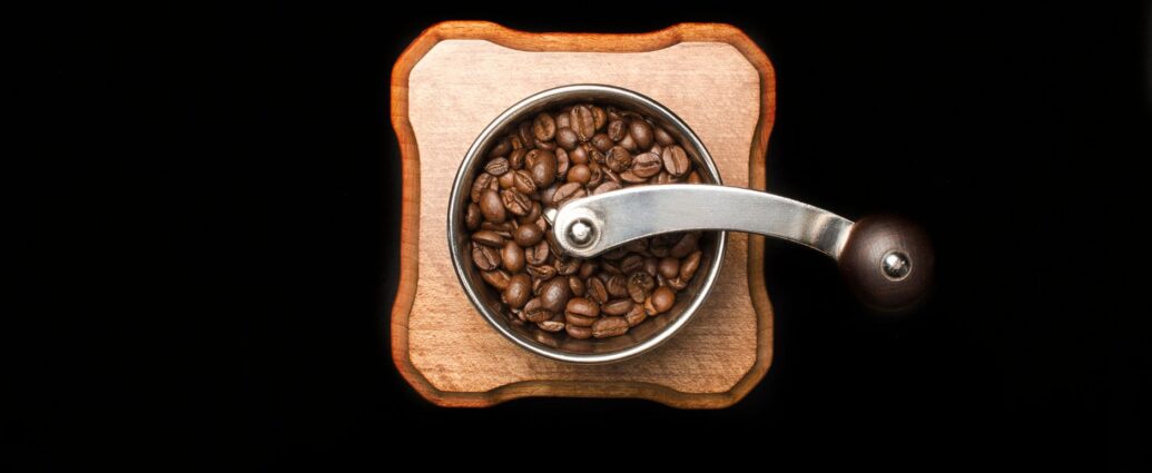 Râșniță manuală de cafea pe o masă de lemn, cu boabe prăjite împrăștiate în jur