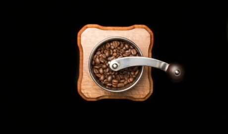 Râșniță manuală de cafea pe o masă de lemn, cu boabe prăjite împrăștiate în jur