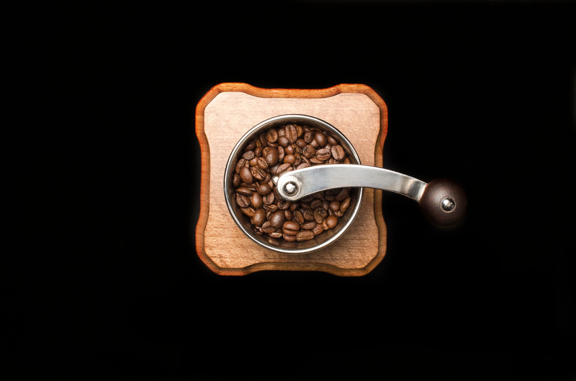Râșniță manuală de cafea pe o masă de lemn, cu boabe prăjite împrăștiate în jur