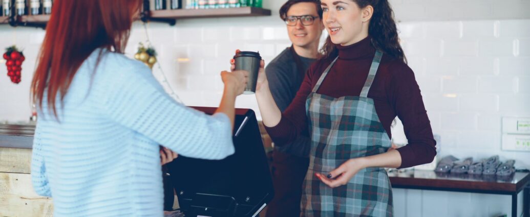 Barista care servește o ceașcă de cafea la tejgheaua unei cafenele, lângă aparatul de espresso